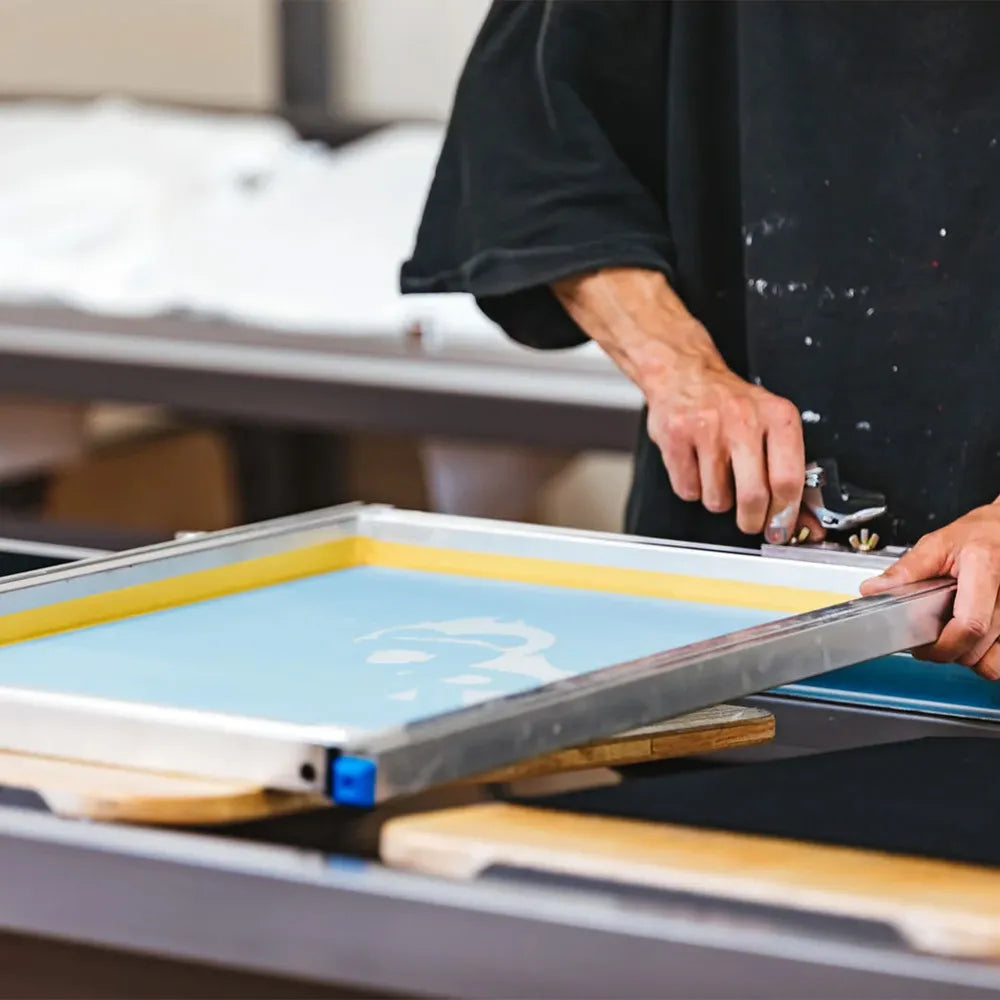 シルクスクリーン印刷でスキージを使い、メッシュフレーム上のインクを均一に伸ばしている作業風景。